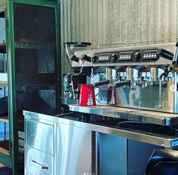 The espresso machine on the stainless steel bench against the corrugated iron wall