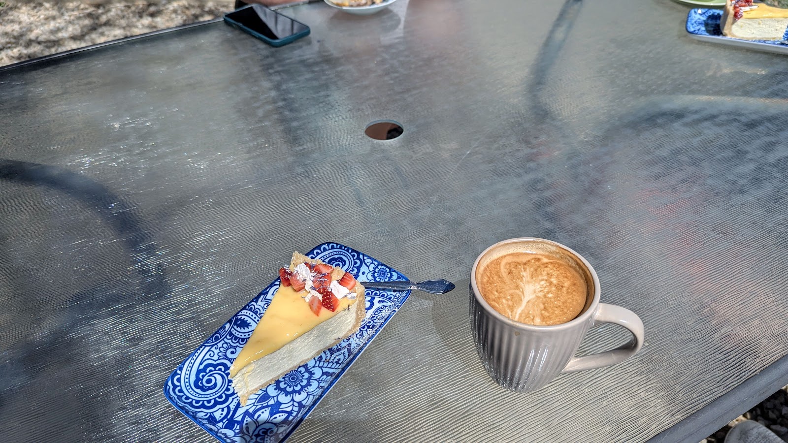 A slice of cheesecake and a coffee on a garden table