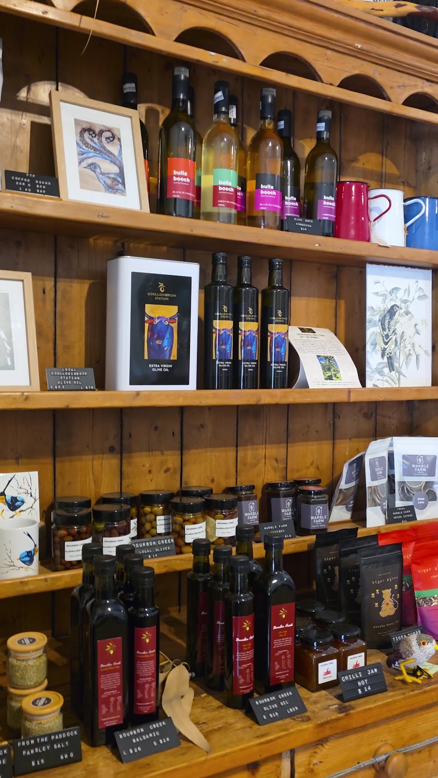 Timber shelves stocked with olive oils, preserves and local goods, with framed art above