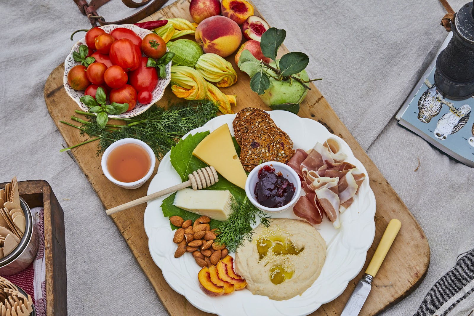 A grazing board with tomatoes, figs, peaches, cheese, cured meats, hummus and honey