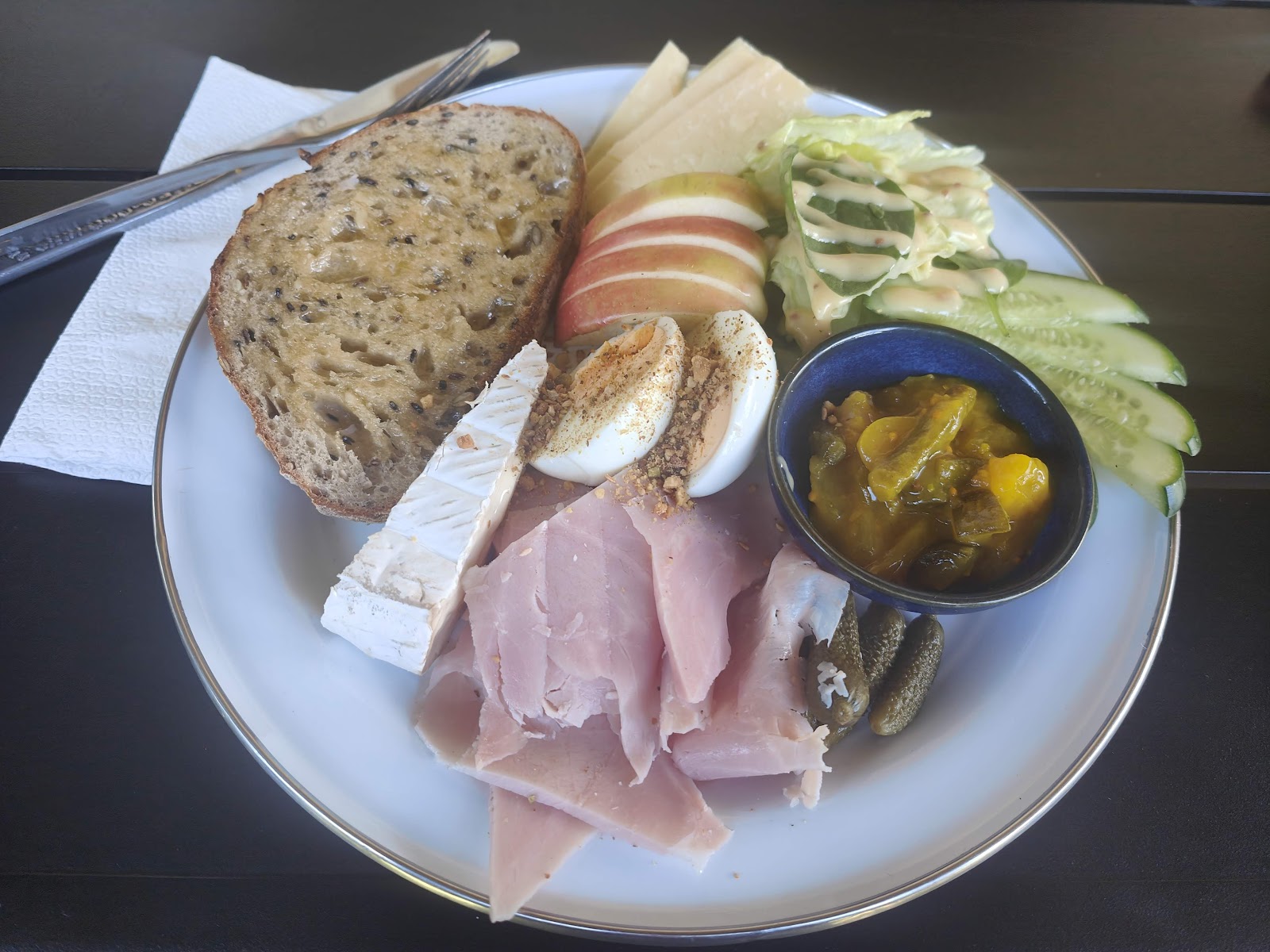 A ploughman's plate with sourdough, ham, egg, brie, apple and pickles